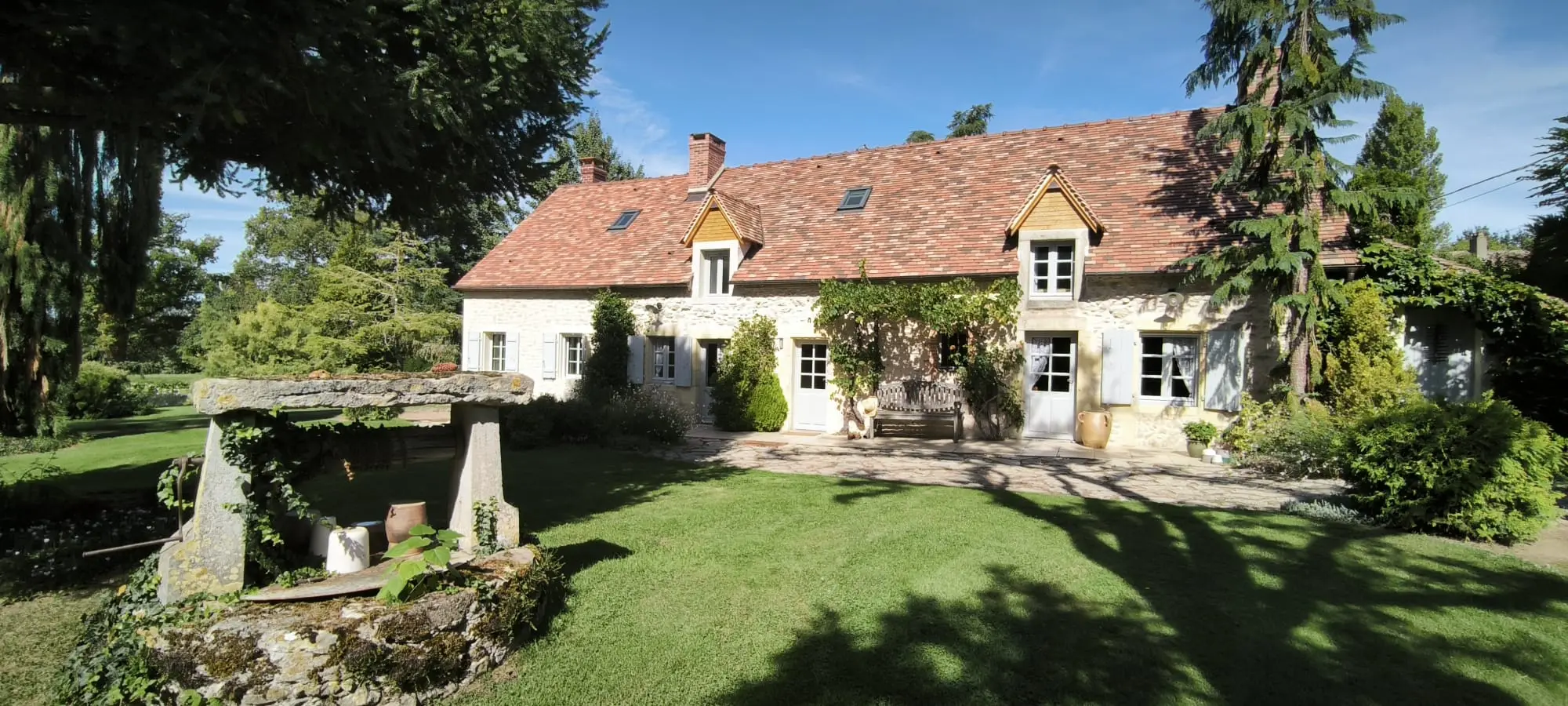 La longère nivernaise aux murs clairs et au toit de tuiles, vue depuis la pelouse